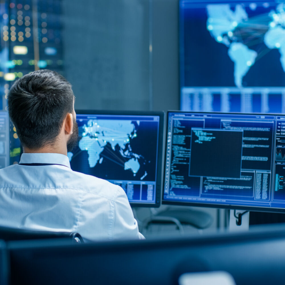 Back View in the System Control Center Operator Working. Multiple Screens Showing Technical Data.
